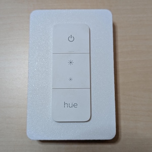 May include: A white Philips Hue smart light switch with a power button, two brightness buttons, and the word "hue" printed on the bottom button.