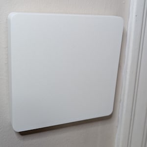 Puede incluir: Una placa de pared cuadrada blanca montada en una pared blanca.