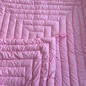 Peut inclure: Une couverture matelassée rose avec un motif carré. La couverture est faite d'un matériau doux et moelleux et a un léger éclat.