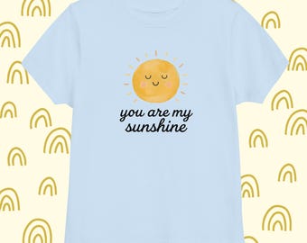 Może przedstawiać: Jasnoniebieska koszulka z uśmiechniętym żółtym słońcem i napisem "you are my sunshine" czarną czcionką. Koszulka wykonana jest z miękkiego materiału, idealna dla dzieci.