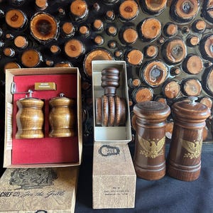 May include: Wooden salt and pepper grinders and shakers, displayed with a nutcracker and boxes. The grinders and shakers are brown with a classic design. The boxes have text that reads "CHEF Spice Mills For the Grill".