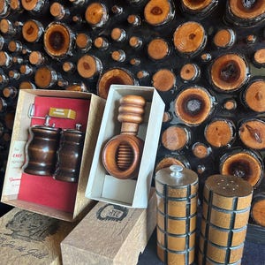 May include: Wooden kitchenware set including a pepper grinder, salt and pepper shakers, and a nutcracker, all in their original boxes. The items are made of dark and light brown wood. The boxes have text and illustrations.