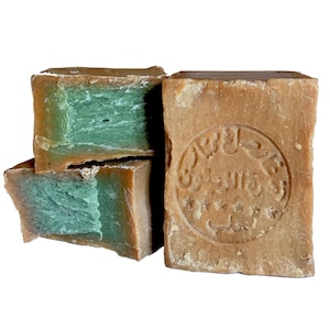 May include: Three bars of brown soap with green inside. The largest bar has a circular stamp with Arabic text.