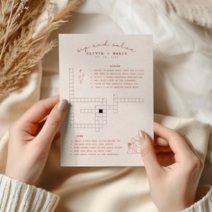 Puede incluir: Una tarjeta de juego de boda de color crema con el texto "sip and solve" y los nombres "Olivia + Marco" en un estilo manuscrito. La tarjeta presenta un crucigrama con pistas relacionadas con la pareja y la fecha "07.19.2027".