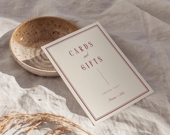May include: A rectangular sign with the words "CARDS and GIFTS" in burgundy lettering, framed by a burgundy border. A ceramic bowl with a speckled design and dried grass are also in the image. The sign also says "THANK YOU!" and has two names.