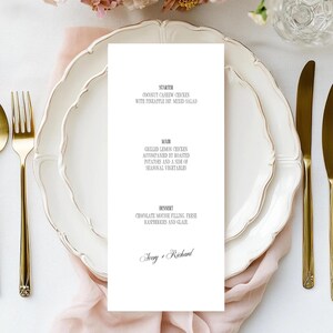 Puede incluir: Elegante tarjeta de men&uacute; de boda con fondo blanco y texto negro. El men&uacute; incluye opciones de entrantes, plato principal y postre. Cubiertos dorados y platos blancos con borde festoneado dispuestos sobre una tela rosa. El men&uacute; est&aacute; personalizado con los nombres "Avery + Richard".