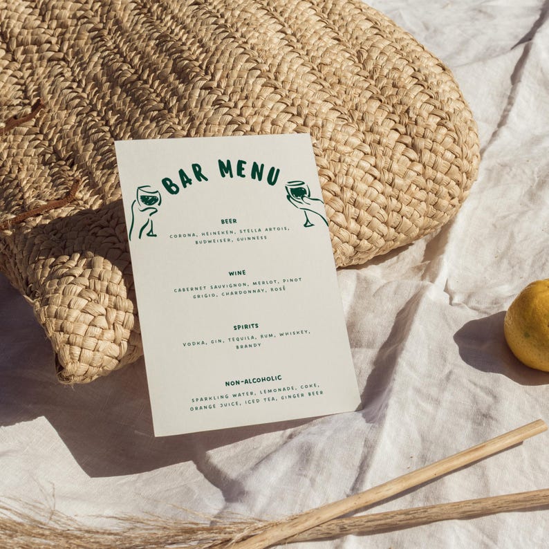 May include: A bar menu with green text and illustrations, listing beer, wine, spirits, and non-alcoholic beverages. The menu is on a white card, with a woven bag and a lemon in the background.