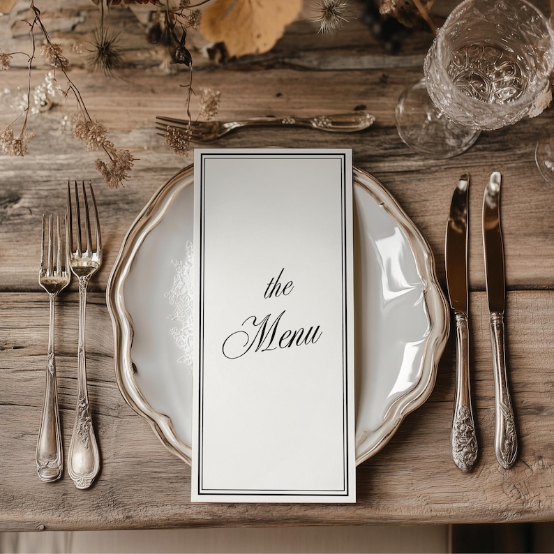 Puede incluir: Una mesa formal con un plato blanco, cubiertos y una tarjeta de men&uacute; que dice "the Menu". La tarjeta del men&uacute; est&aacute; centrada en el plato, con cuchillos y tenedores a cada lado. La mesa es de madera.