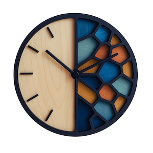 Op de afbeelding: Een ronde wandklok met een marineblauw frame. De linkerkant is licht hout en de rechterkant heeft een geometrisch ontwerp met blauwe, oranje en turquoise accenten. Zwarte wijzers en markeringen maken het ontwerp compleet.