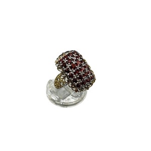 May include: A gold and silver ring with a rectangular red gemstone setting. The ring is set with many small red gemstones.