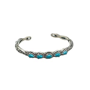 May include: A silver cuff bracelet with a delicate, intricate design and turquoise stones.