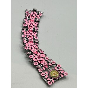 May include: A pink and silver floral bracelet with a large pink flower and a green stone in the center.