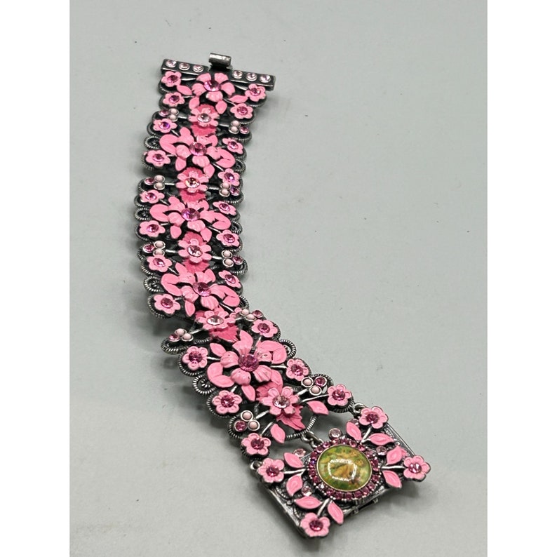 May include: A pink and silver floral bracelet with a large pink flower and a green stone in the center.