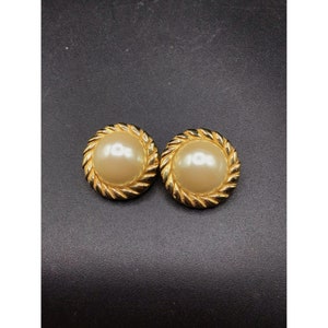 May include: A pair of gold tone earrings with a faux pearl center. The earrings have a rope-like design around the edge.