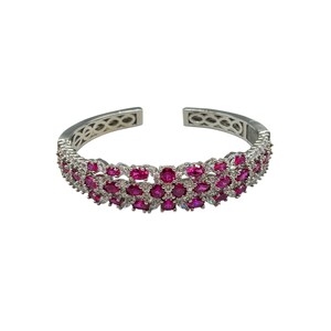 May include: A silver-toned cuff bracelet with two rows of oval-shaped, deep pink gemstones. The bracelet has an open design and is set against a white background. The gemstones are arranged closely together, creating a continuous band of color.