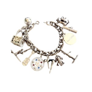 May include: A silver charm bracelet with a variety of charms, including a frog, a diver, a guitar, a number 16 charm, a gymnast, a surfer, a dog, a house, a ball, and a charm with the inscription "June 2, 1968".