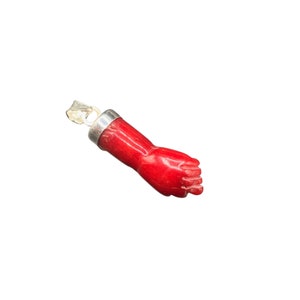 Puede incluir: Un colgante de mano de coral rojo con una anilla de plata. La mano está tallada en un estilo realista y tiene un dedo y un pulgar detallados.