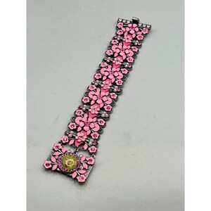 May include: A pink and silver floral bracelet with a green stone in the center. The bracelet is made of metal and has a delicate design.
