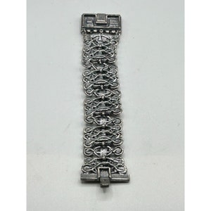May include: A silver bracelet with a detailed, intricate design. The bracelet is made of linked chains with a clasp closure.