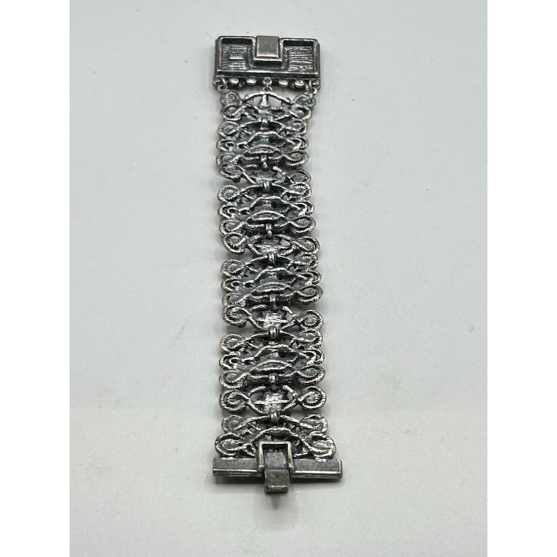 May include: A silver bracelet with a detailed, intricate design. The bracelet is made of linked chains with a clasp closure.
