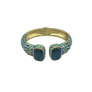May include: Gold-tone cuff bracelet with blue and teal gemstones. The bracelet features two large, square, dark blue gemstones at the opening and is encrusted with smaller blue and teal stones. The bracelet is open at the bottom.
