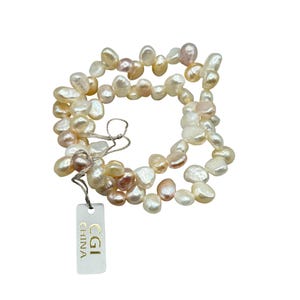 Peut inclure: Un brin de perles d'eau douce de couleur blanc cassé, crème et rose pâle. Les perles sont de forme irrégulière et présentent un léger reflet irisé. Les perles sont enfilées sur un fil blanc fin et sont reliées par une petite étiquette blanche sur laquelle est inscrit "CGI CHINA".