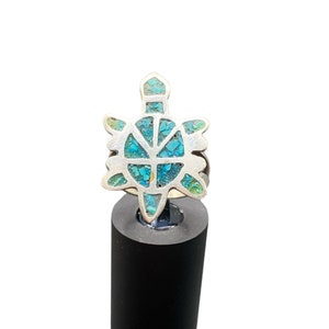 May include: A silver ring with a turquoise turtle design. The turtle is outlined in silver and the shell is filled with turquoise stones.