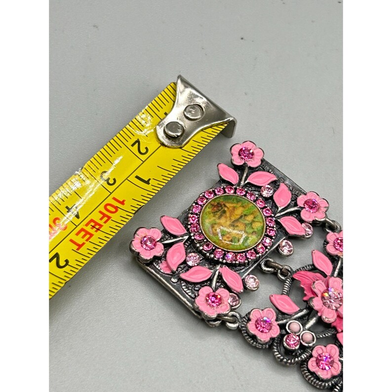 May include: A silver charm with a pink enamel floral design and a green and gold cameo. The charm is decorated with pink rhinestones.