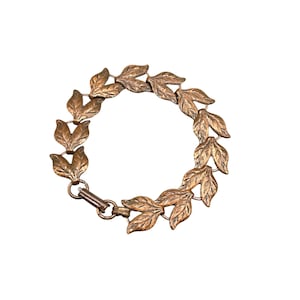 May include: A copper bracelet with a leaf design. The bracelet is made of individual leaves that are linked together.