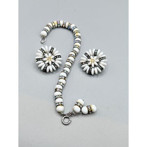 Può includere: Un set di gioielli vintage con un braccialetto di perline bianche e orecchini a forma di margherita abbinati. Il braccialetto e gli orecchini hanno accenti di strass iridescenti. Gli orecchini e il braccialetto hanno una chiusura argentata.