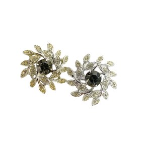 May include: A pair of silver tone earrings with a swirl design. Each earring features a black rhinestone in the center surrounded by smaller clear rhinestones and silver leaves.