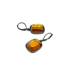 May include: A pair of lever-back earrings featuring large, faceted, amber-colored rectangular stones set in dark gray metal. The earrings are displayed against a white background, showcasing their design and color.