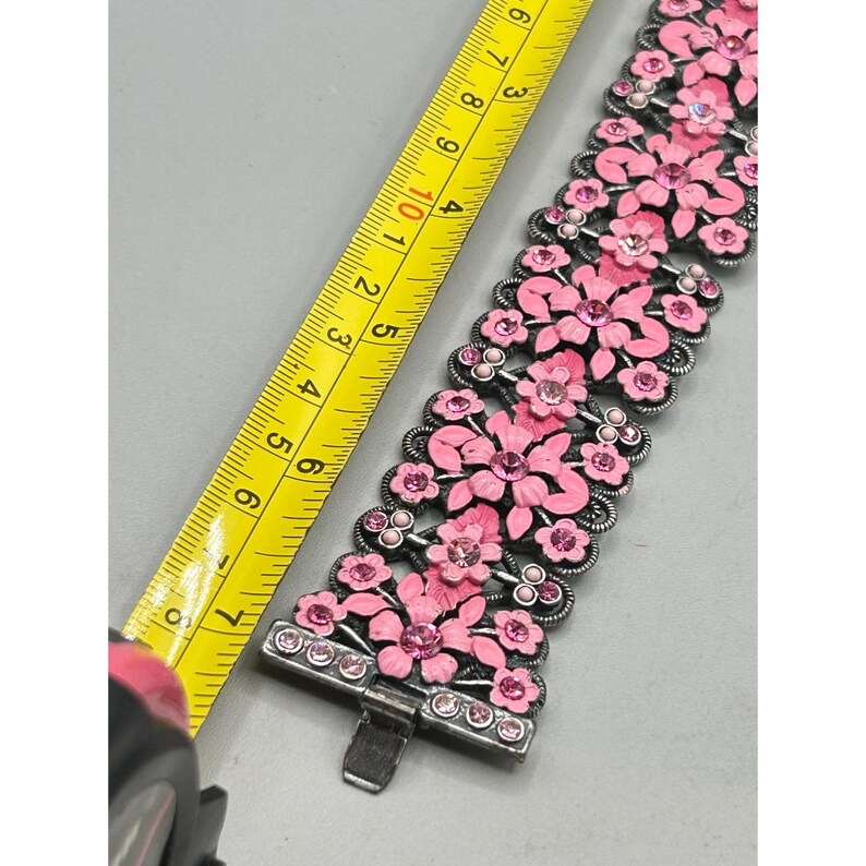 May include: A silver bracelet with a floral design. The flowers are pink and have rhinestones in the center. The bracelet is about 7 inches long.
