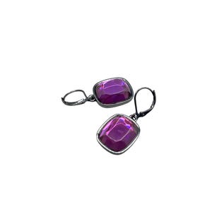 May include: A pair of earrings featuring large, square-cut, iridescent purple gemstones set in a dark metal frame. The earrings have a lever-back closure. The gemstones reflect light, creating a shimmering effect.