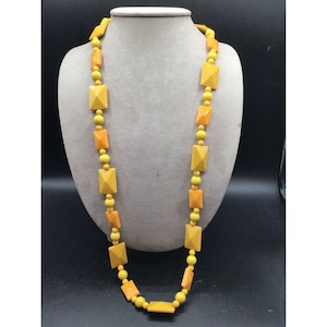 May include: A long yellow and orange beaded necklace with square-shaped beads. The necklace is on a mannequin.