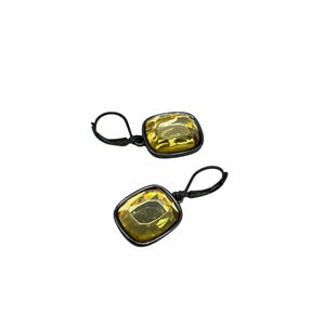 May include: A pair of earrings featuring large, square-cut, yellow gemstones set in black metal frames. The earrings have a lever-back closure. The gemstones have a reflective quality, catching the light.