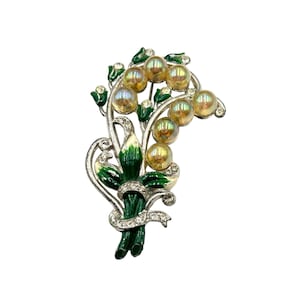 Op de afbeelding: Een zilverkleurige broche met een cluster van iriserende gele glazen kralen, ingelegd in een groen emaille bloemenontwerp.