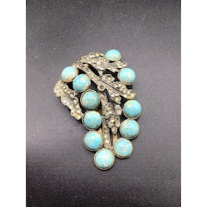 Pode incluir: Um broche vintage com um cacho de pedras cabochão azul turquesa engastadas em um metal prateado com um design de folhas. O broche é adornado com strass transparentes.