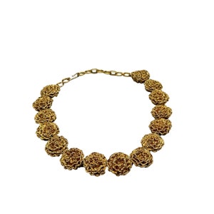 May include: A gold necklace with a chain and a series of round, textured, flower-shaped charms.