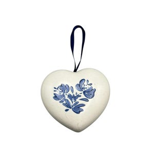 Op de afbeelding: Witte keramische hartvormige ornament met een blauw bloemenmotief en een blauw lint om op te hangen.