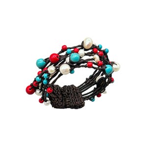 May include: A multi-strand bracelet featuring a woven brown clasp and strands of dark brown cord. The bracelet is adorned with red, turquoise, and white beads, including large pearl-like beads. The beads are interspersed throughout the design.
