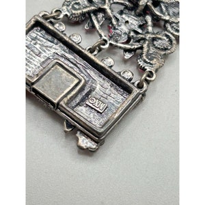 May include: Close-up of a silver bracelet with a floral design and pink rhinestones. The clasp is visible and has the inscription "&copy;XW" on it.
