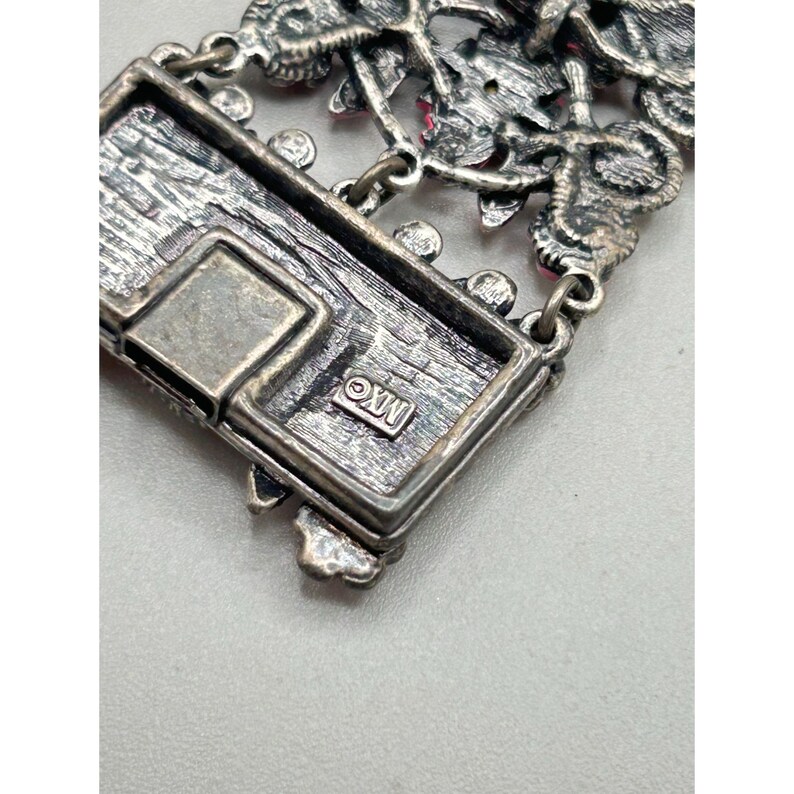 May include: Close-up of a silver bracelet with a floral design and pink rhinestones. The clasp is visible and has the inscription "&copy;XW" on it.