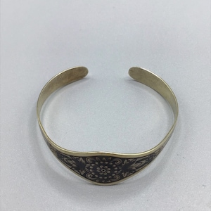 Op de afbeelding: Een gouden armband met een zwart bloemenmotief.