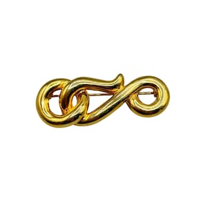 May include: A gold-toned metal brooch in the shape of an infinity symbol. The brooch is made of two interlocking loops.