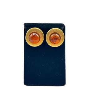 May include: A pair of gold tone earrings with amber glass cabochons. The earrings are displayed on a black velvet background.