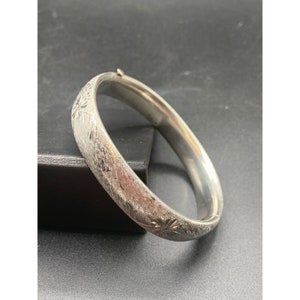 May include: A silver bangle bracelet with a floral design. The bracelet is made of polished silver and has a simple, elegant design.