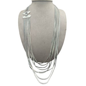 Puede incluir: Un collar de plata de múltiples cadenas con un cierre único. El collar está hecho de múltiples cadenas finas que se superponen.