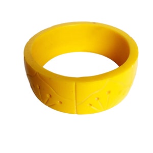 May include: A bright yellow bangle bracelet with a floral design. The bracelet is made of a smooth, hard plastic.