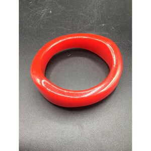 Op de afbeelding: Een felrode plastic armband. De armband is glad en glanzend.